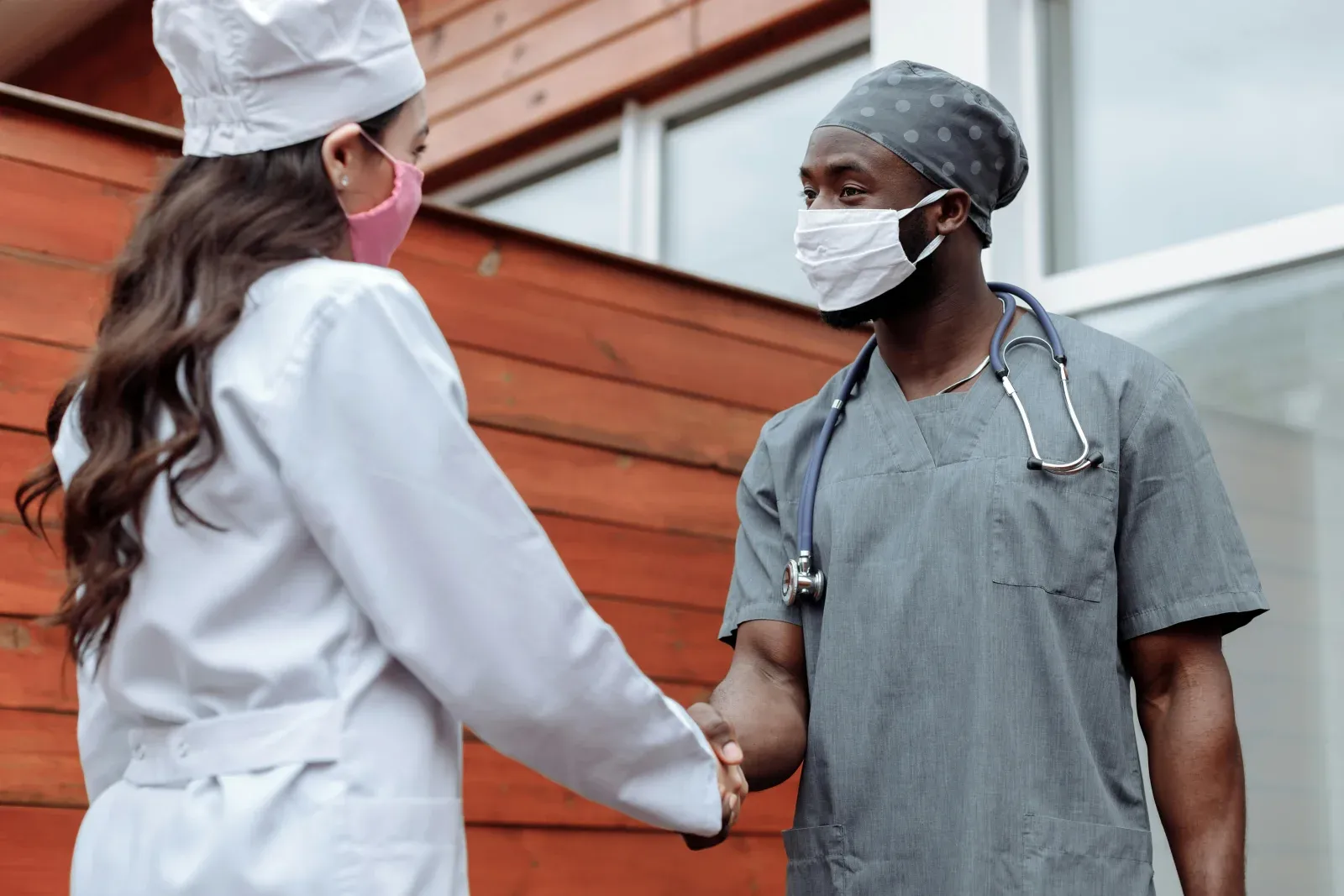 Two healthcare professionals shaking hands outside a workplace.